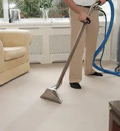 Professional carpet cleaner using a hot-water extraction wand and hose machine in a living room in Cape Coral, FL.