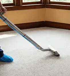 Steam carpet cleaning technician using a hot-water extraction wand on a residential carpet, wearing blue protective shoe covers Cape Coral, FL.