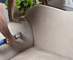 Professional upholstery cleaner deep-cleaning a fabric sofa with a handheld extraction tool and hose in Cape Coral, FL.